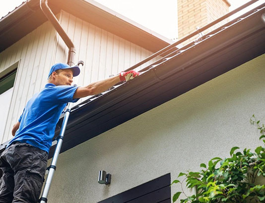 Man on ladder cleaning house gutter from leaves and dirt